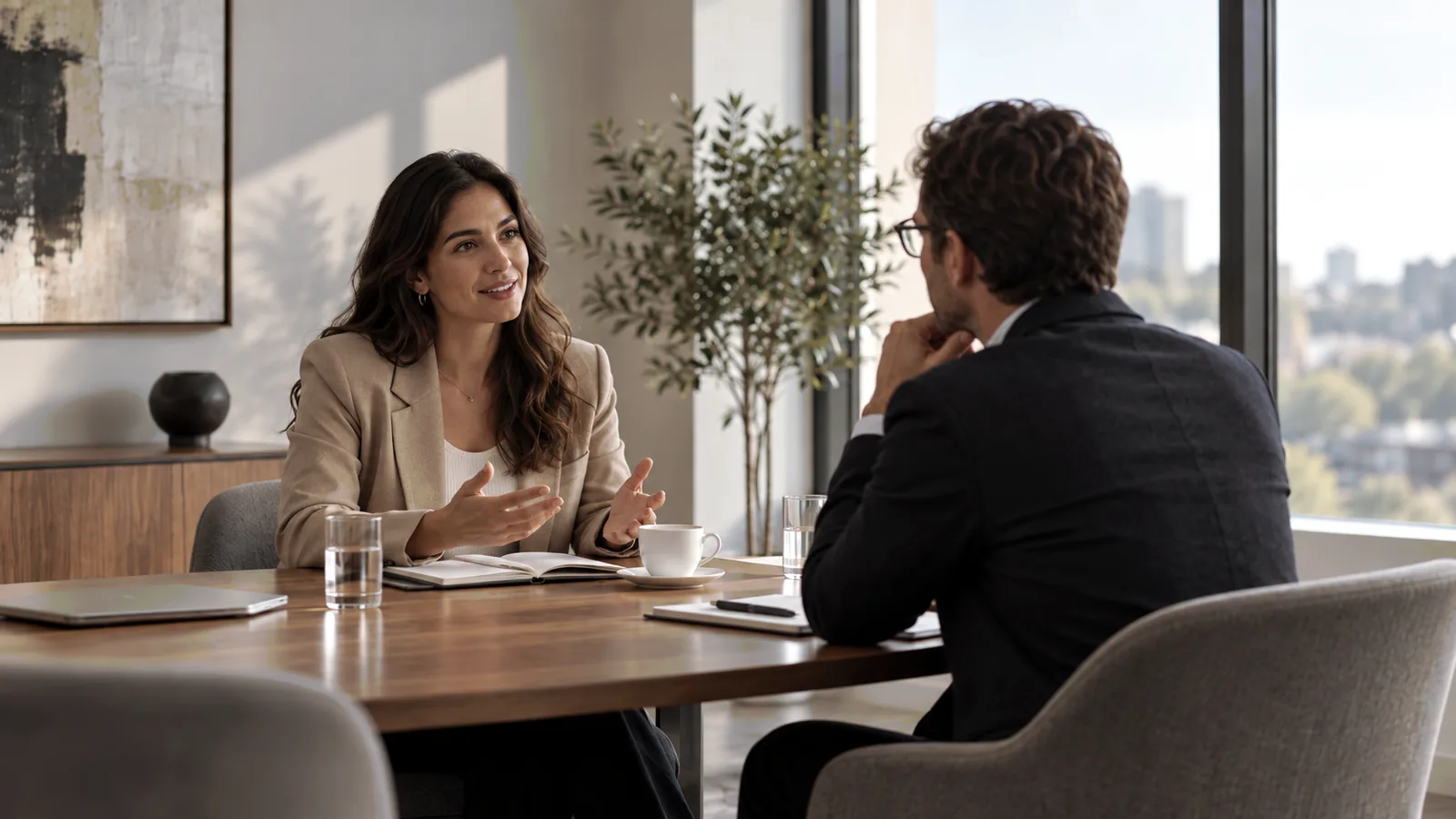 Duas pessoas conversando à mesa, em sala de reunião com luz natural.